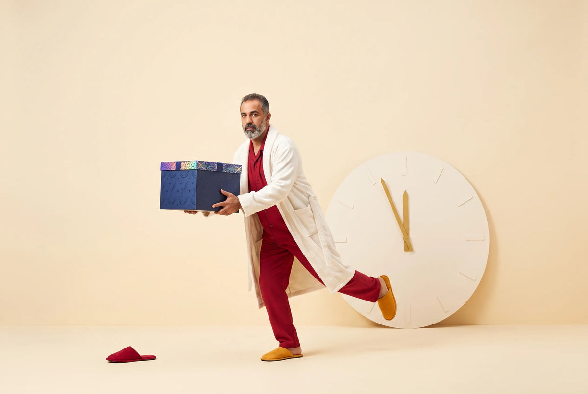 A man in red pajamas and a white robe hurries with a navy Everwow gift box past a large clock with both hands near twelve