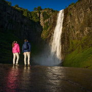 Two hikers gazing up at a tall waterfall in a green gorge, Chasing Waterfalls experience gift