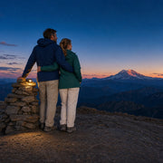 Couple standing close at a summit cairn at dusk lit by a headlamp, Peak Moments experience gift