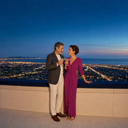 Couple toasting cocktails at a rooftop rail above the lit LA basin, Anniversary in Los Angeles experience gift