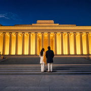 Two visitors gazing up at a grand illuminated colonnade at dusk, Architecture Tours experience gift