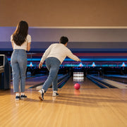 Man bowling a hot pink ball toward the pins as his partner watches, Bowling & Arcades experience gift