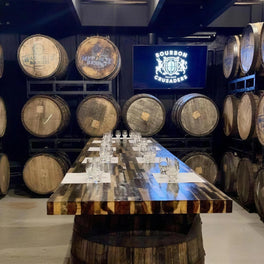 Long tasting table set with glasses in a whiskey cellar lined with oak barrels