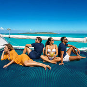 Four friends relaxing on a catamaran trampoline over turquoise water, Catamaran Party Cruise experience gift
