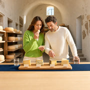 Couple tasting cheese wedges at a cellar counter lined with wheels, Cheese Tasting experience gift