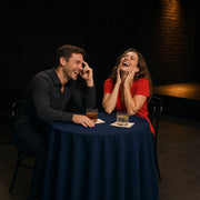 Couple laughing hard at a spotlit club table near the stage, Comedy Shows experience gift