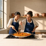Student stirring saffron rice as an instructor adds paprika in a sunlit kitchen, Spanish Cooking Classes experience gift