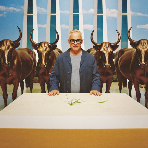 Man standing at a white plinth in front of bronze longhorn statues and a painted sky backdrop