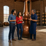 Guide explaining a copper still to a couple holding whiskey glasses, Distillery Tour experience gift
