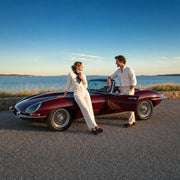 Couple leaning beside a burgundy vintage roadster on a coastal byway, Vintage Wheels experience gift