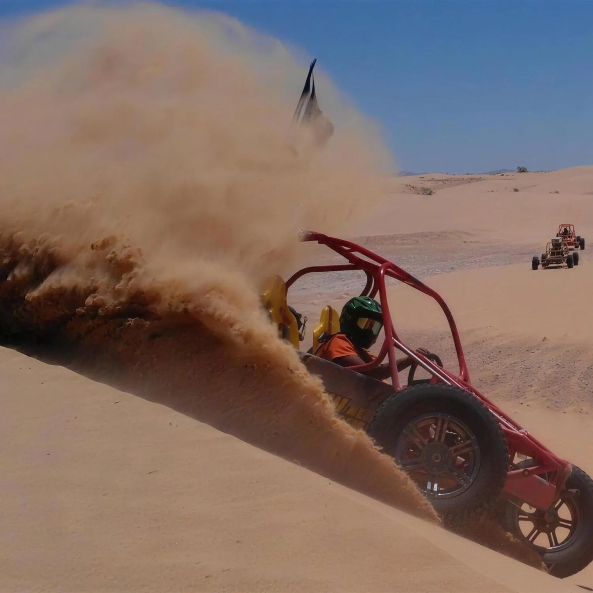 Red dune buggy throwing up a plume of sand as it speeds across a desert dune