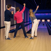 Three friends celebrating a strike at a neon bowling alley, Shared Laughs experience gift