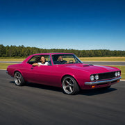 Father and adult daughter grinning in a magenta muscle car on a sunlit track, Superdad experience gift