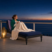Woman curled on a chaise with warm tea on a sea-view balcony at dusk, Quiet Escape experience gift