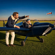 Child at the controls of a parked plane as a parent points down the grass runway, Junior Pilot experience gift
