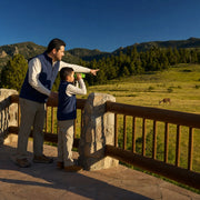 Child watching a deer through binoculars at a park overlook as a parent points, Junior Ranger experience gift