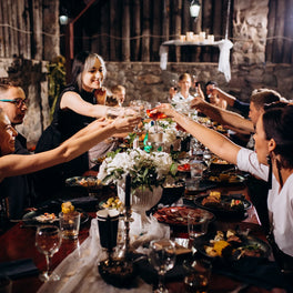 Family and friends toasting around a long candlelit table laid for a celebration dinner
