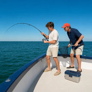 Son fighting a bent fishing rod as his father readies the net at the boat rail, Fishing experience gift