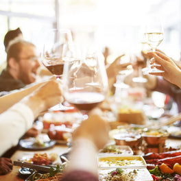 Friends raising wine glasses in a toast over a table of shared dishes
