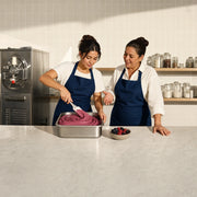 Student folding berry gelato in a steel tub with her instructor, Gelato Making Class experience gift