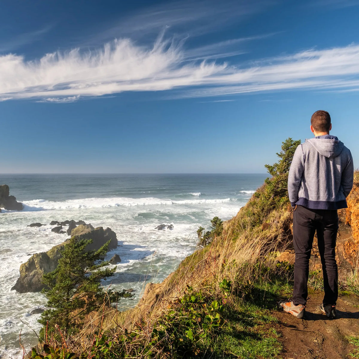 Walker on a grassy clifftop path looking out over rocky sea stacks and open water