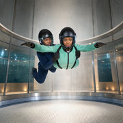 Instructor steadying a flyer floating in a vertical wind tunnel, Indoor Skydiving experience gift