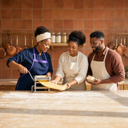 Chef-instructor rolling fresh pasta with a couple in a warm kitchen, Italian Cooking experience gift