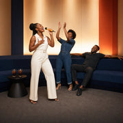 Friend belting a note into the mic as two others cheer in a karaoke room, Karaoke experience gift