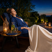 Woman unwinding on a spa lounger at dusk beside a lantern, Retreat Glow experience gift