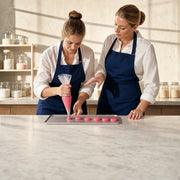 Student piping macaron shells beside her instructor in a studio, Macaron Making Class experience gift