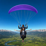 Tandem pilot and passenger soaring over a valley under a violet canopy, Paragliding experience gift