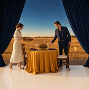 Woman carrying a roast platter to a harvest table in a golden field, Iconic Happy Thanksgiving experience gift