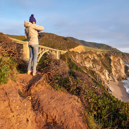 Couple embracing on a clifftop viewpoint above a coastal bridge and the ocean at sunset