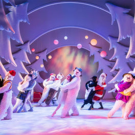 Performers in white costumes on a brightly lit stage during a seasonal theatre show