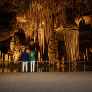 Two visitors gazing up at vast stalactites in a warm-lit cavern, Explore the underworld experience gift