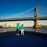 Two passengers at the bow of a sightseeing boat nearing a suspension bridge, Sail Away experience gift
