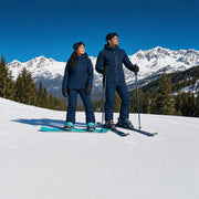 Couple pausing mid-run on a sunlit piste with snow-capped peaks behind, Skiing & Snowboarding experience gift
