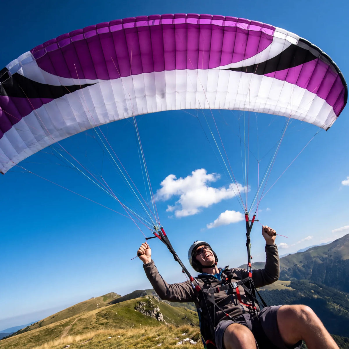 Paraglider under a purple canopy soaring above green mountain ridges and blue sky