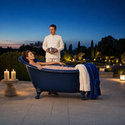 Woman reclining in a petal-topped clawfoot tub on a garden terrace at dusk, Spa Day Magic experience gift