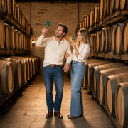 Couple raising tasting glasses among oak barrels in an aging room, Spirits & Distillery Tours experience gift
