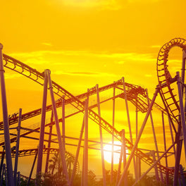 Silhouetted rollercoaster track against a bright orange sunset at a theme park