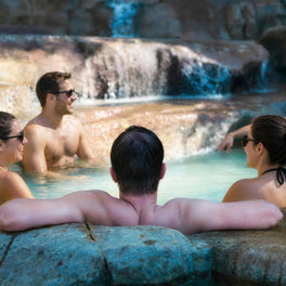 Bathers relaxing in a steaming natural hot spring pool beside a small waterfall