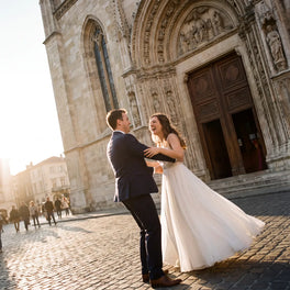 Groom lifting a laughing bride outside a gothic cathedral in golden evening light