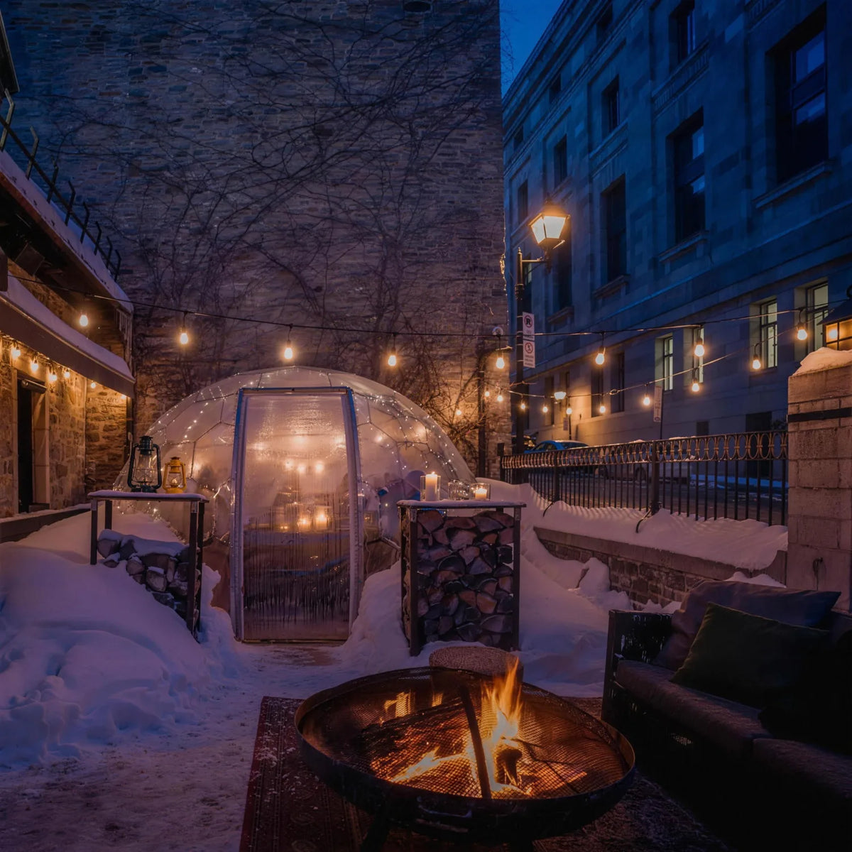 Snow-covered courtyard with a fire pit and a lit glass dining dome for a winter dinner