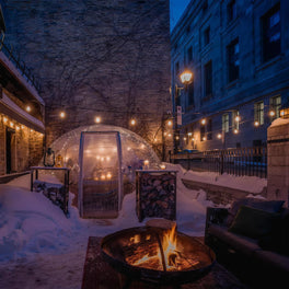 Snow-covered courtyard with a fire pit and a lit glass dining dome for a winter dinner