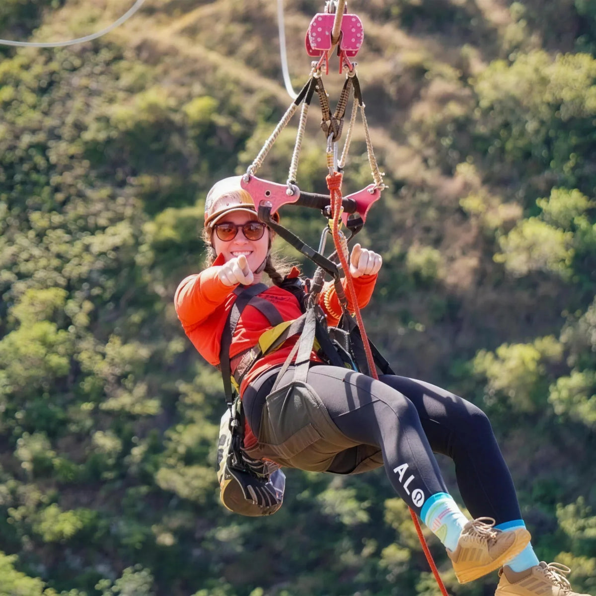 Zip line rider in helmet and harness gliding above a forested valley