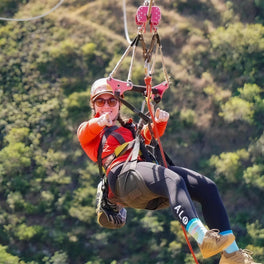 Zip line rider in helmet and harness gliding above a forested valley