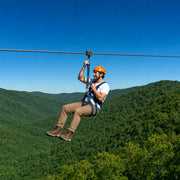 A rider gliding a steel zip line high above a green forest canopy, Zip Lining experience gift
